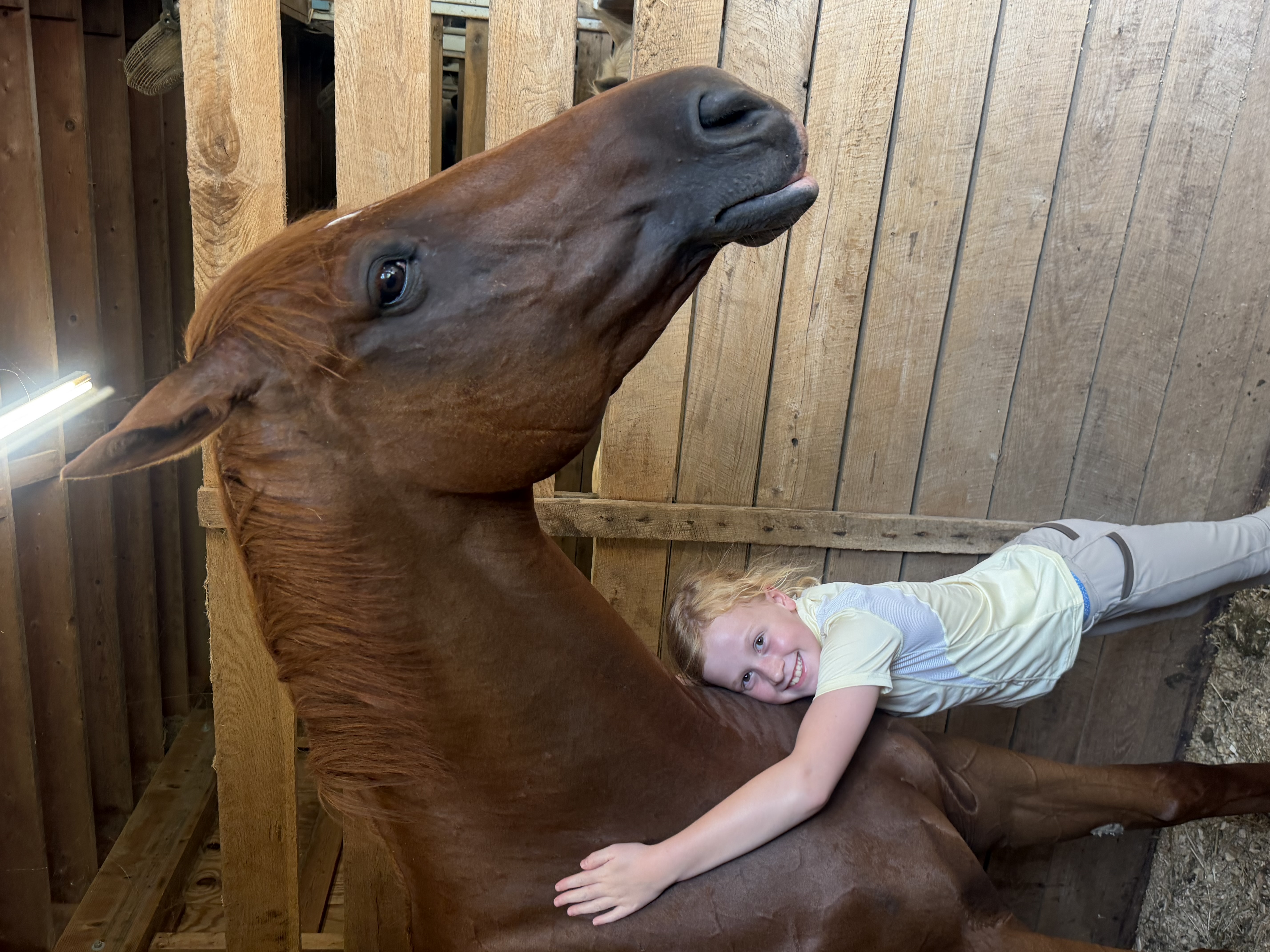 A smiling young rider standing beside a lesson horse in the barn