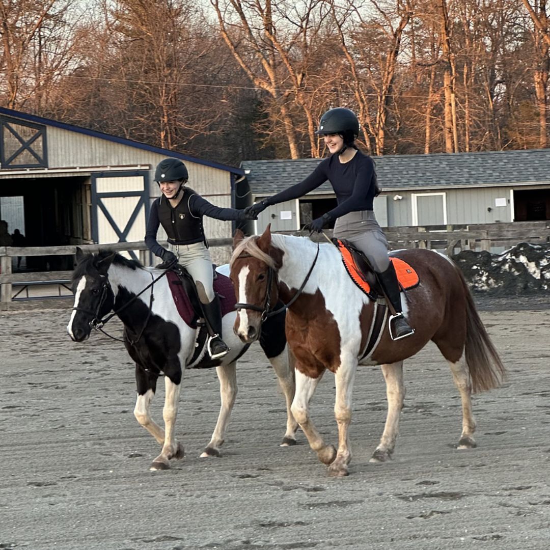 A smiling young rider standing beside a lesson horse in the barn